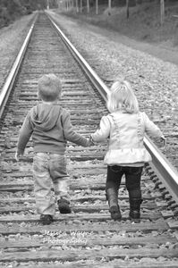 a little boy and girl walking hand in hand along train tracks