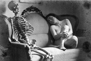 Nude woman on a couch looking at a skeleton