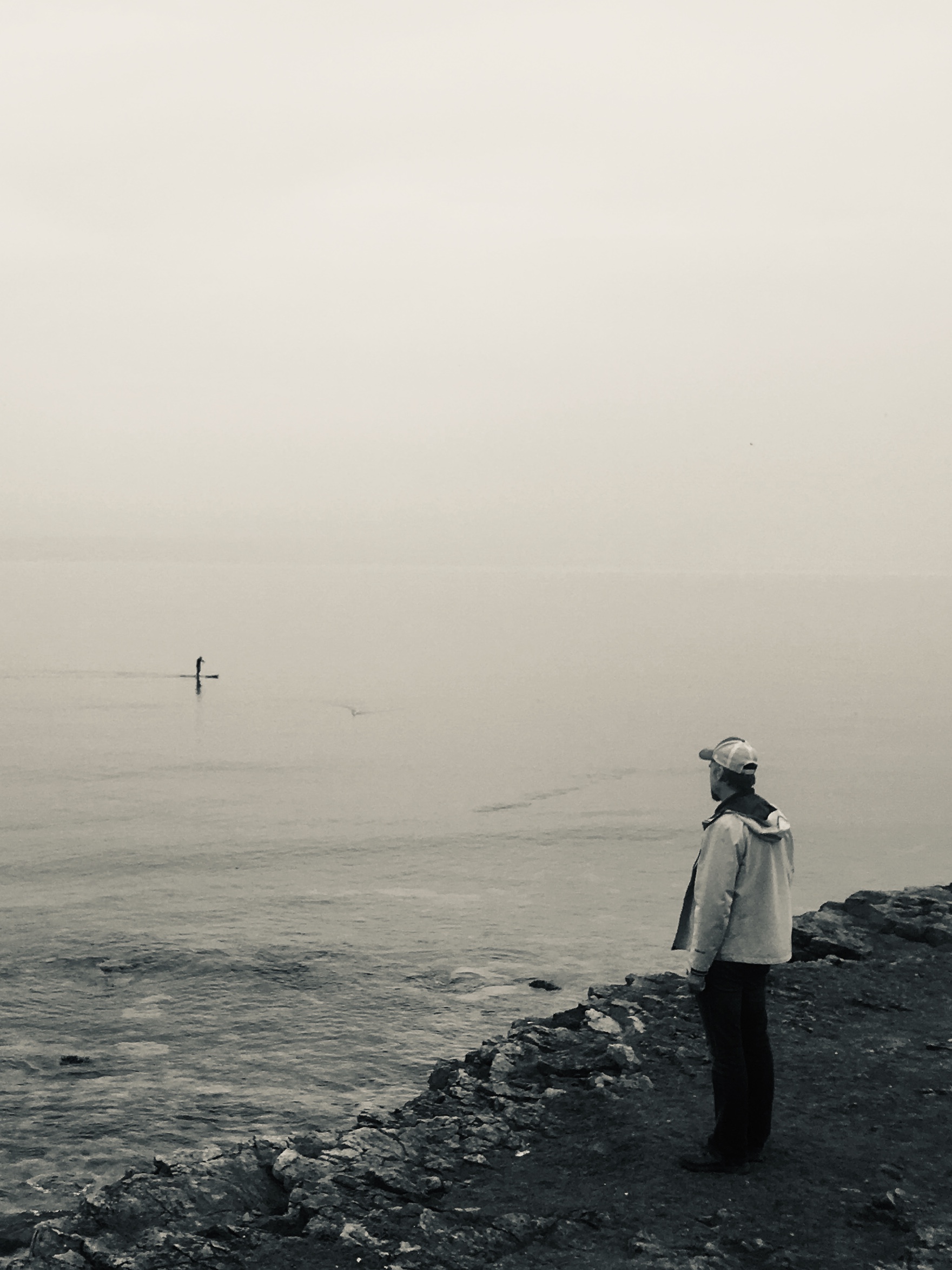 A man standing on a cliff looking out at the water