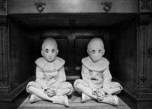 Two children in identical costumes with masks under a desk