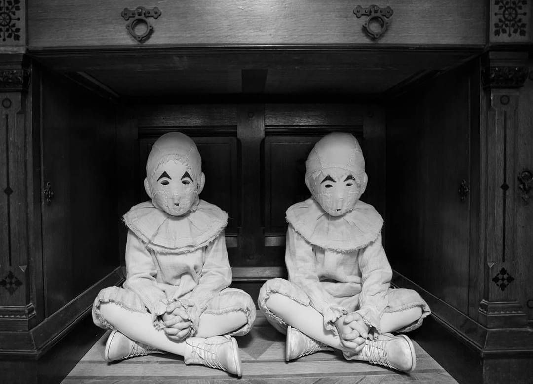 Two children in identical costumes with masks under a desk