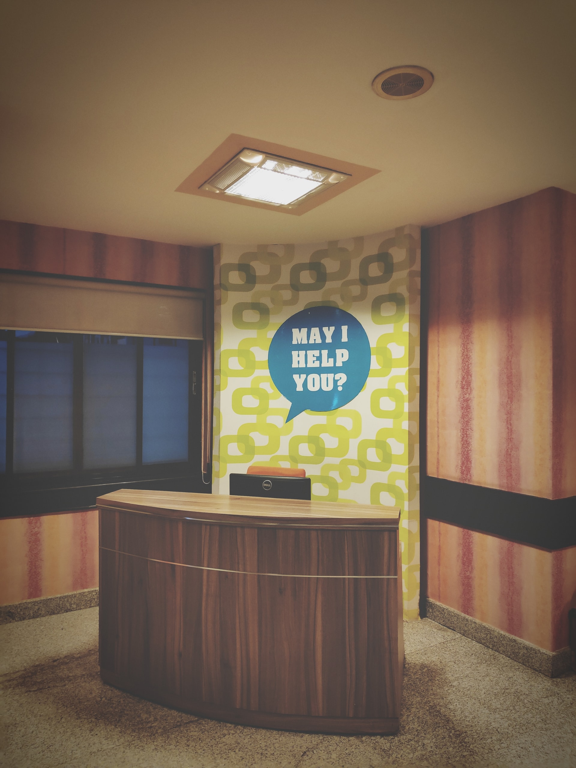 reception desk with a "may I help you" sign 