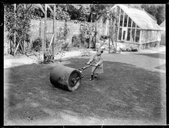 Little boy pushing a large piece of machinery across the yard