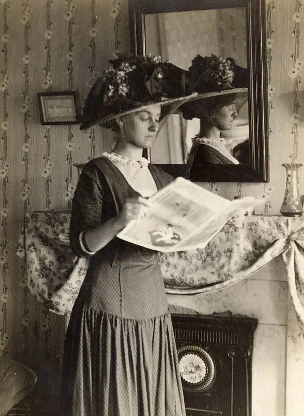 A woman standing reading a newspaper in 1910.