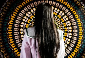 a woman with long hair facing a tapestry
