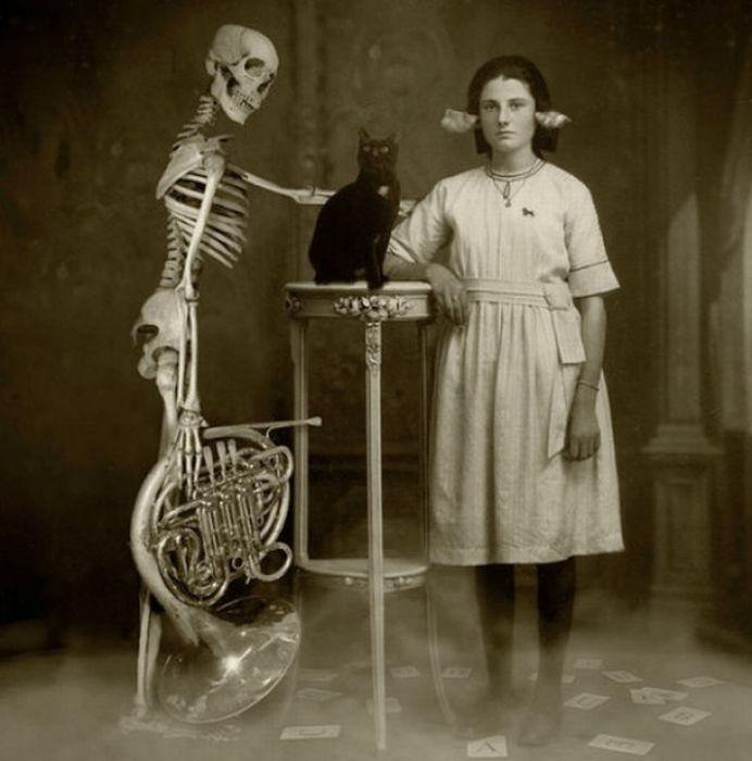 Vintage photo of a woman leaning on table with a black cat standing next to a skeleton holding a trombone.