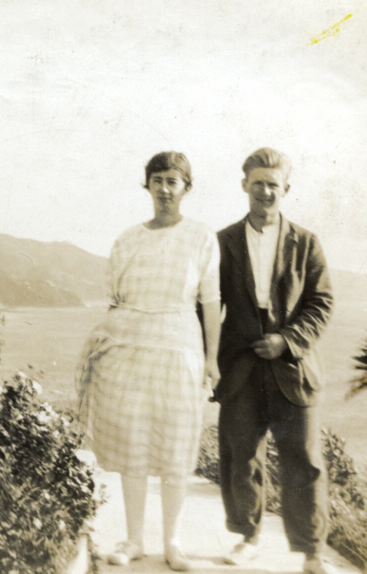 Image shows a bride and groom standing outside. A child can be seen watching the photograph be taken from steps on the left hand side of the image.