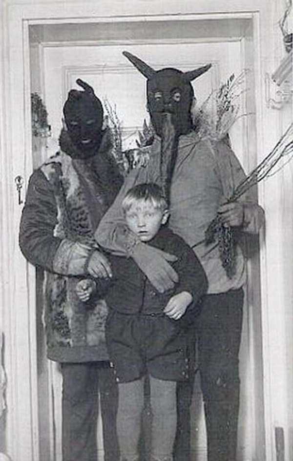 Vintage photo of two people in bizarre costumes clutching a scared boy