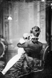 vintage photo of a woman holding a baby with a skull for a head.