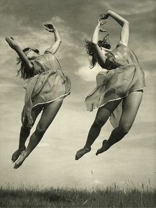 Photo of two women in summer dresses leaping into the air